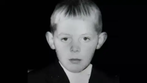 A black and white picture of a young Henry Cunningham. He is wearing a white shirt and black jacket. You can tell he has blond hair and his ears stick out.