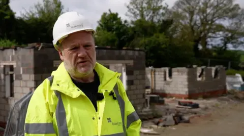 John Freeland standing on a building site, wearing a high-visibility jacket and a hard hat