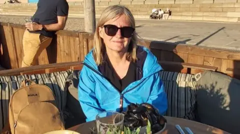 Jan Palmer A woman in a blue coat sits outdoors at a table with a bowl of mussels