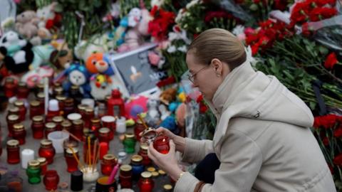 A woman lights a candle at a makeshift memorial to the victims of a shooting attack set up outside the Crocus City Hall concert venue in Moscow (24/03/24)