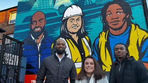 Milton Walcott, Rosa Wells and D’ontae Rock stand in front of a mural featuring their likenesses.