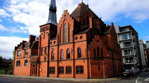 Tiger A view of the Scandinavian Seamen's Church on the corner of Park Lane and Cornhill in Liverpool's docklands. The Gothic design has a tall spire and stepped gables, and has reddish-brown bricks.