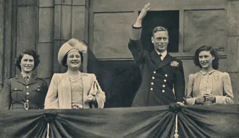 Getty Images The King, Queen and Princesses Elizabeth and Margaret are smiling from the Royal Balcony at Buckingham Palace. King George VI and Princess Elizabeth are wearing military uniform. The Queen and Princess Margaret are dressed formally.