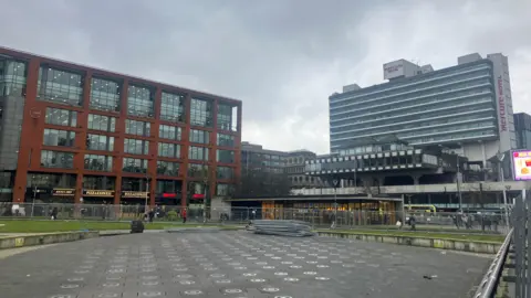 Metal fencing can be seen around Piccadilly Gardens, with a pile of railings laid on the ground.