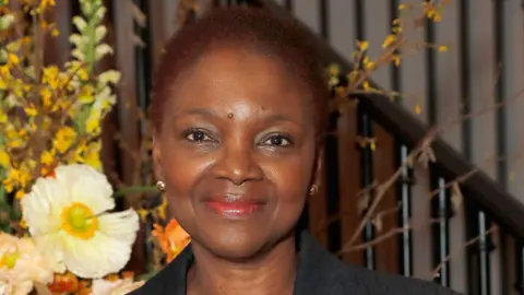 Getty Images Baroness Amos attending an event. She is wearing a black blazer, with flowers behind her
