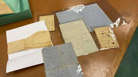 University of Gloucestershire Poems handwritten on old pieces of paper, as well as a cotton beige night cap, are laid out on a brown wooden table.