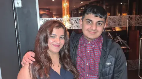 Family handout Pooja and Ronan are standing outside a restaurant. Both are smiling with Rona's arm around his mother. She has long dark hair and a sleeveless top on and Rona has a checked shirt on and a black jacket.