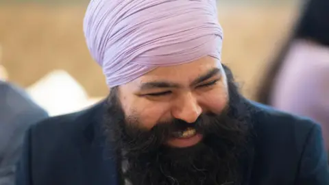 Handout Kuljit dressed in a blue blazer and lilac turban smiling and looking away from camera 