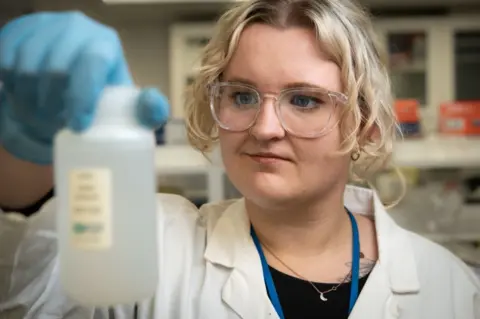 Tony Jolliffe/BBC PhD researcher Laura Taylor holds a small bottle of water containing meltwater from an iceberg