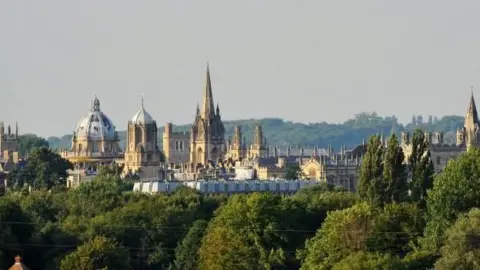 Oxford skyline showing college buildings and church spires above many trees in summer leaf