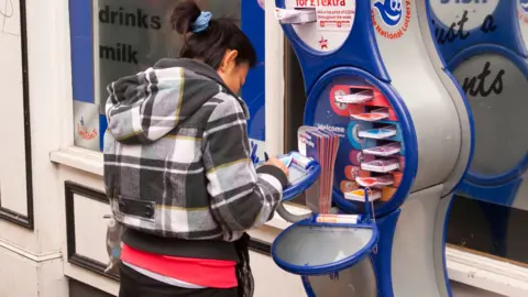 Alamy A woman fills out a form for a National Lottery ticket at a stand outside a shop