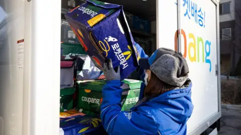 Getty Images A Coupang employee wearing a protective mask unloads an eco-bag carrying fresh food from a delivery truck in Bucheon
