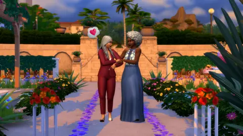 Electronic Arts An in-game screenshot from the game The Sims 4, showing two women walking down the aisle holding each others arms. One woman, with tan skin, in a burgundy suit, has a love heart above her head in a thought bubble. The other woman, who is black with curly grey hair, is wearing a blue and white dress and smiling.