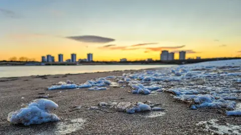 Mercuryblue/BBC Weather Watchers The frozen chunks cover the sand on a beach near Aberdeen. The city's tower blocks are almost silhouetted against a yellow sky.