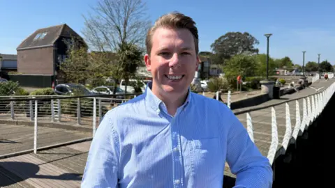 A man with a blue shirt smiling in the sunshine. 