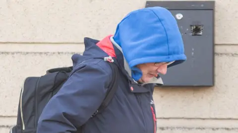 Pacemaker Amanda Fulton is photographed with her caput  down   and wearing a bluish  hoodie with the hood pulled up. She has a achromatic  backpack connected  and wearing a navy coat. 