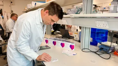 Steve Roest with short black hair in a white lab coat looking at a test strip