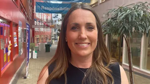 Susie Davis smiles at the camera. She has long, straight brown hair and is wearing a black top.