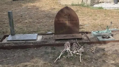 Kay Mason Billig Three graves can be seen desecrated, with parts of the headstone ripped off, in a churchyard with dry grass around it.
