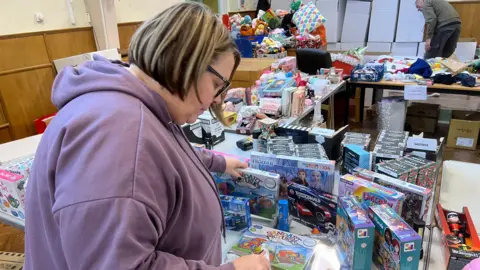 A volunteer wearing a purple hoodie sorting through boxed toys