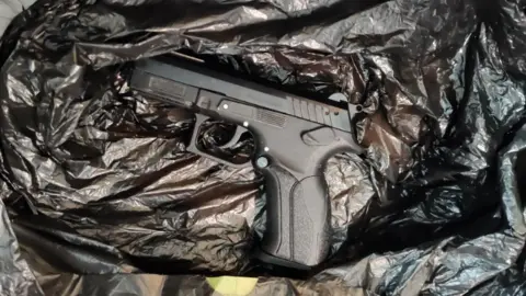 Greater Manchester Police The black pistol recovered by police lies side-on, muzzle to the left, in an opened black bin bag. It looks in good condition.
