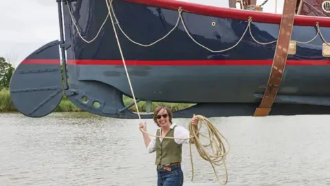 A woman standing in front of a boat that's being held in the air
