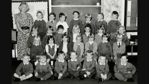 A black and white school photo showing smiling pupils and their teacher.
