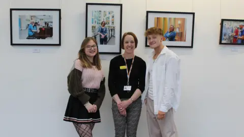UWE Carla, Donna and Kian standing beside their framed photographs at the exhibition