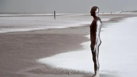Ron Davies A close up of one of the Antony Gormley’s Iron Men sculpture on Crosby beach with the other ones in the background.