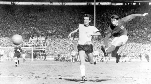 Getty Images Sir Geoff Hurst is pictured mid-air as he kicks the ball in England’s final goal in the World Cup final in 1966. 