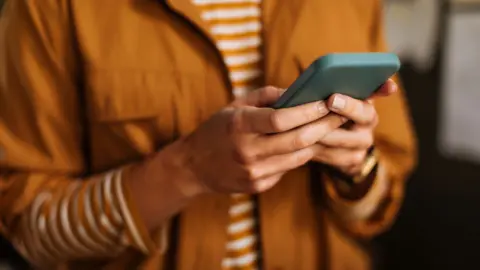 Torso of someone in brown shirt holding their mobile phone 