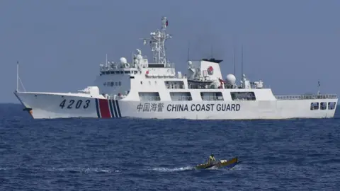Getty Images A China Coast Guard ship monitors a Philippine fisherman aboard his wooden boat during the distribution of fuel and food to fishers by the civilian-led mission Atin Ito (This Is Ours) Coalition, in the disputed South China Sea on May 16, 2024