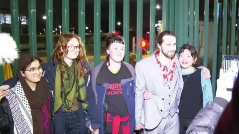 Charlotte Head, Leona Kamio, Fatema Rajwani, Zoe Rogers and Jordan Devlin stood outside in the dark with a green, metal fence behind them