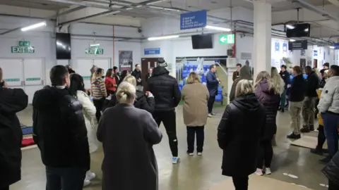 Light Project Peterborough People standing inside the Peterborough United ground listening to an event organiser.