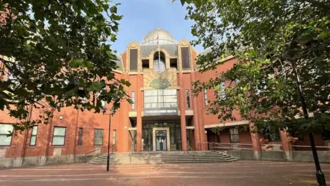 Exterior of Hull Crown Court a red brick building with a central glass dome with steps leading up to the main entrance and a paved forecourt with trees