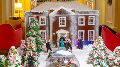 Steve Adams/Assembly House A close-up shot of the gingerbread model, which shows a Georgian-style house topped with snow and decorated Christmas trees and two igloos in its snowy front garden, laid out on a table inside The Assembly House and surrounded by chairs.