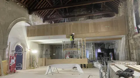 Shaun Whitmore/BBC Work being completed to the interior of Norwich Castle. A builder stands on scaffolding and appears to be fixing wood panelling to a wall. Stacks of wood are piled up on side of the room