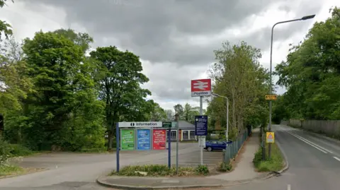 An exterior view of Poynton railway station in Cheshire. The entrance to the station is at the side of a road bridge which runs over the railway line.