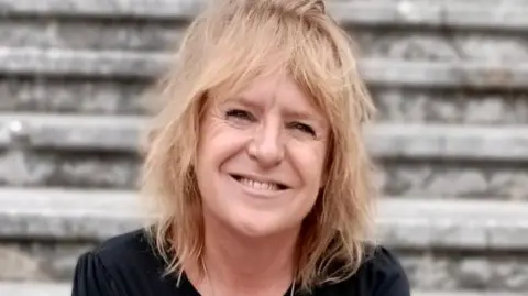 INQUEST Deborah Coles wearing a black T-shirt and smiling. She has shoulder-length blonde hair.