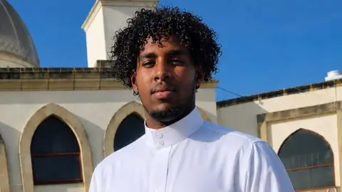 A man wearing white with curly dark hair and facial hair.