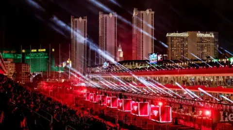     EPA-EFE/REX/Shutterstock is at the F1 Grand Prix in Las Vegas. Rays of light can be seen from one level of the stands. There are illuminated boxes around a basement, and three towers can be seen in the background.