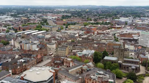 Aerial view over Wolverhampton with buildings across the city and hills and sky in the background.