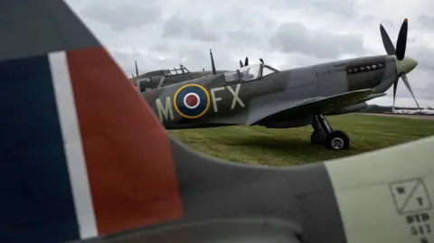 Getty Images A Spitfire on the ground at an aerodrome. There are other aircraft visible in the background and foreground. 