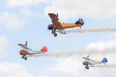 PA Real Life Three bi-planes in flight with wing walkers Flame Brewer, 21, Rose Powell, 20, and Jasmine Norman, 20 on the top deck of each aircraft.