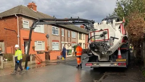 Two workers on a street with a water pumping machine