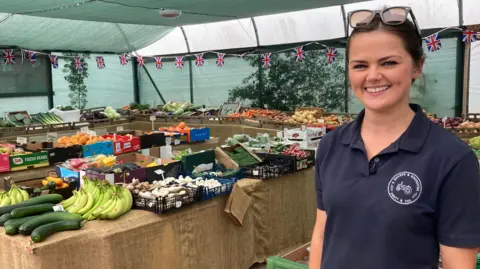 Bethany Sharpe smiling in front of an array of fruit and vegetables in her shop at Langworth near Lincoln