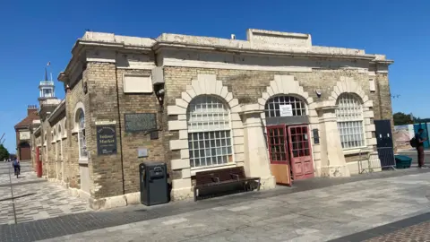 An outside view of the Stockton Shambles building. It has open red doors in the centre of stone archways with windows. 