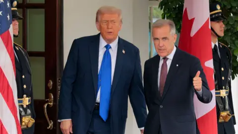 Two men stand between the US and Canadian flags.