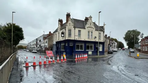 South Eldon Street. There is a line of red and white cones with Road Closed sign next to a two-storey pub called Kennedy's. 