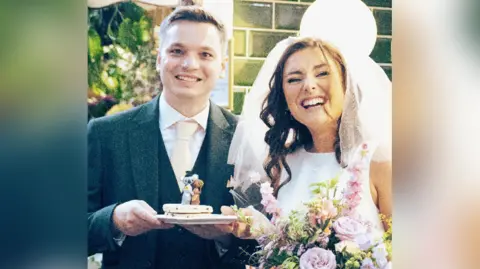 Felixine Hick Harmony and Seán smiling whilst holding a plate with two welsh cakes on and two wedding toppers on top. Harmony is also holding a large bouquet of flowers. 